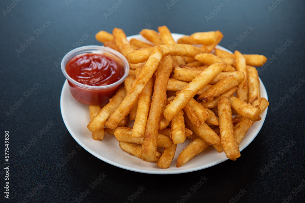 French fries with ketchup on dark background, side view French fries with ketchup on dark background, side view
