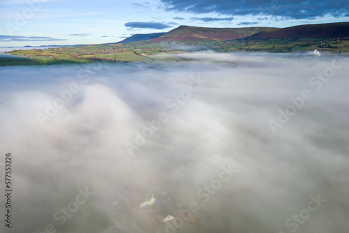 Aerial view flying over a bank of fog over a large large surrounded by mountains (Llangorse Lake, Wales)