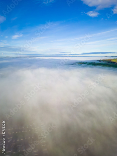 Aerial view flying over a bank of fog over a large large surrounded by mountains (Llangorse Lake, Wales)