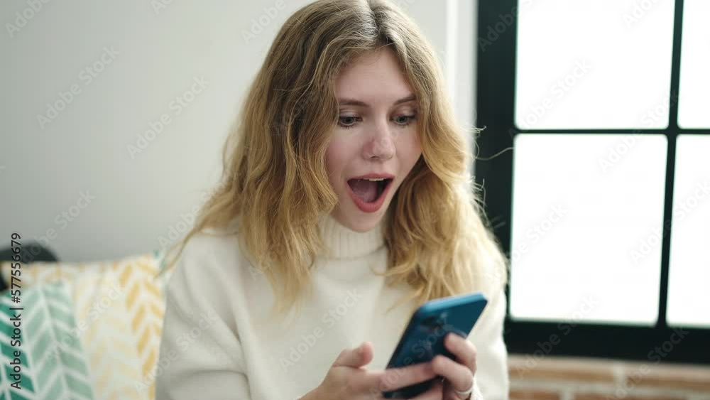 Young blonde woman using smartphone with winner expression at home Young blonde woman using smartphone with winner expression at home