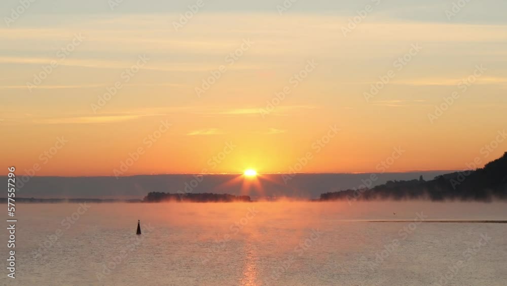 A bright yellow-hot sunrise over a foggy river. The morning sun's rays shimmer in the fog and clouds A bright yellow-hot sunrise over a foggy river. The morning sun's rays shimmer in the fog and clouds