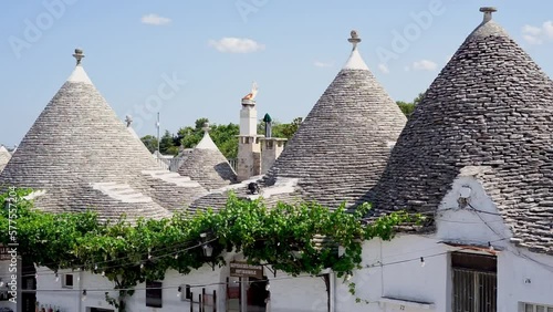 Tourists stroll among Apulian trulli.
Summer holidays in southern Italy. Characteristic trulli houses and people visiting the city on a warm sunny day. photo