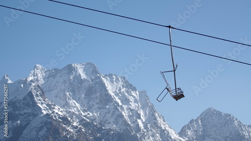 Cable car on background of mountain peaks and blue sky. Creative. Mountain lift with moving empty cabins with snow-capped mountains. Beautiful landscape of snowy rocky mountains and blue sky with