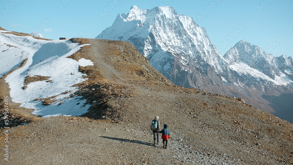 Hiking with child in mountains with snowy peaks. Creative. Mother and boy climb mountains on autumn sunny day. Family hiking in mountains with snowy peaks on sunny day