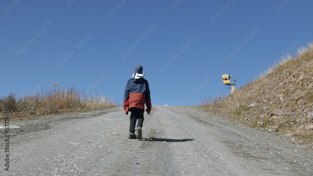 Boy goes up mountain road. Creative. Boy is walking on road uphill. Boy climbs mountains on road on autumn sunny day