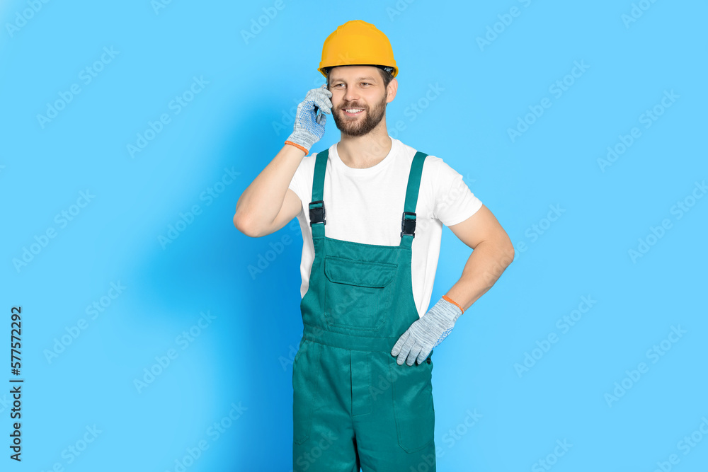 Professional repairman in uniform talking on smartphone against light blue background Professional repairman in uniform talking on smartphone against light blue background
