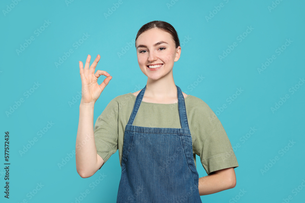 Beautiful young woman in clean denim apron on light blue background Beautiful young woman in clean denim apron on light blue background