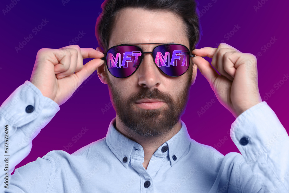 Confident man on color background. Abbreviation NFT reflecting in sunglasses - obrazy, fototapety, plakaty 