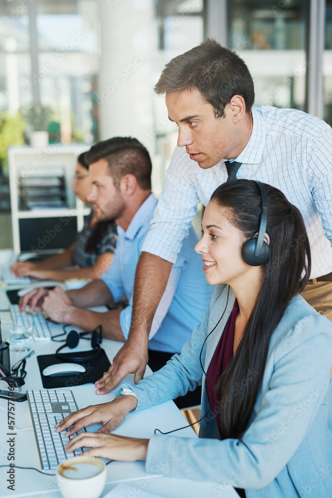 He maintains a visible presence in his department. Shot of a young man assisting his colleague in a call center. He maintains a visible presence in his department. Shot of a young man assisting his colleague in a call center.