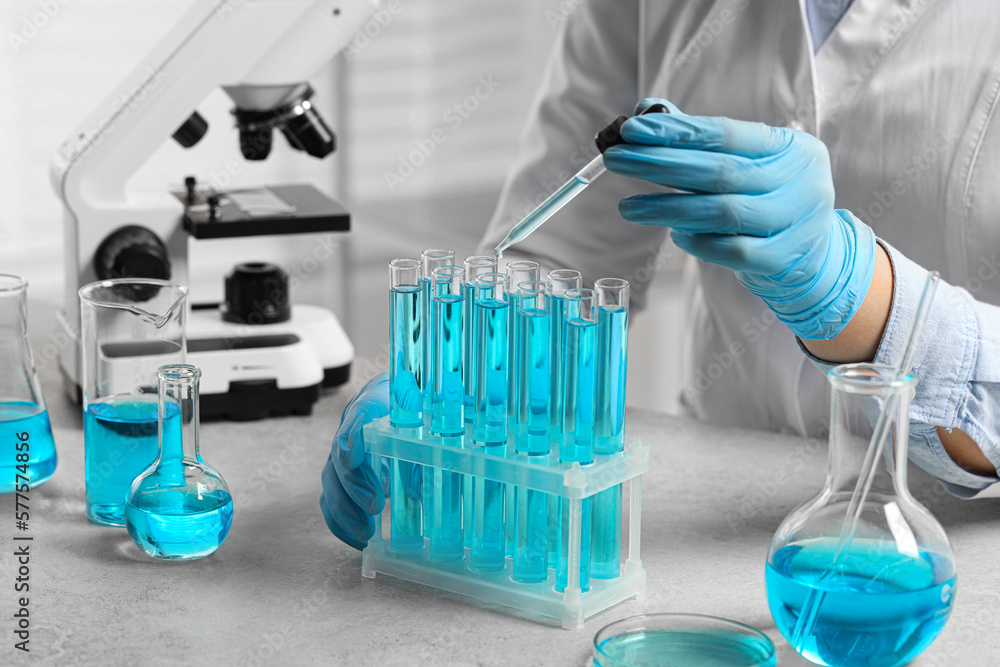 Fototapeta premium Scientist dripping liquid from pipette into test tube at white table in laboratory, closeup