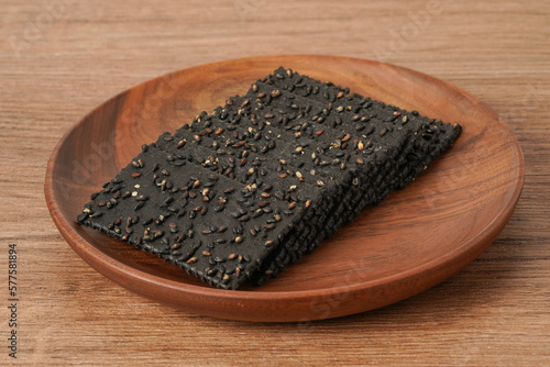 A pile of biscuits made of black sesame lies on a solid wooden table
