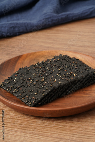 A pile of biscuits made of black sesame lies on a solid wooden table