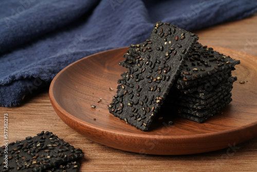 A pile of biscuits made of black sesame lies on a solid wooden table