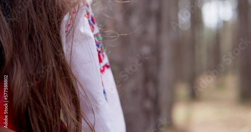 Bulgarian girl in traditional folklore costume red white dress with shevitsa touching with hand trees in forest of majestic mountain, 4k slow motion video. Bulgaria nature. photo