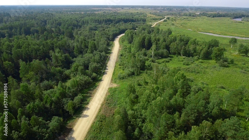 Top view of empty country road with green forest. Stock footage. Panorama of road in forest area with green fields in summer. Summer landscape of country road with green forest and sunny blue sky