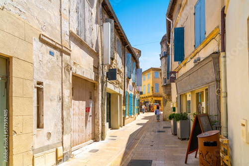 Fototapeta Naklejka Na Ścianę i Meble -  A woman walks down a narrow alley of shops  and apartments through the historic medieval town of Saint-Remy de Provence, France, on a sunny summer day in the Provence, Cote d'Azur region.