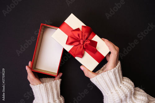 Hands with knitted sleeves hold open gift box on black background