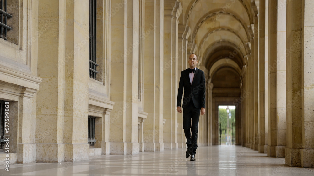 Man in black and white official suit walking in arcuate shaped hall. Action. Man walking outdoors by the building with columns.