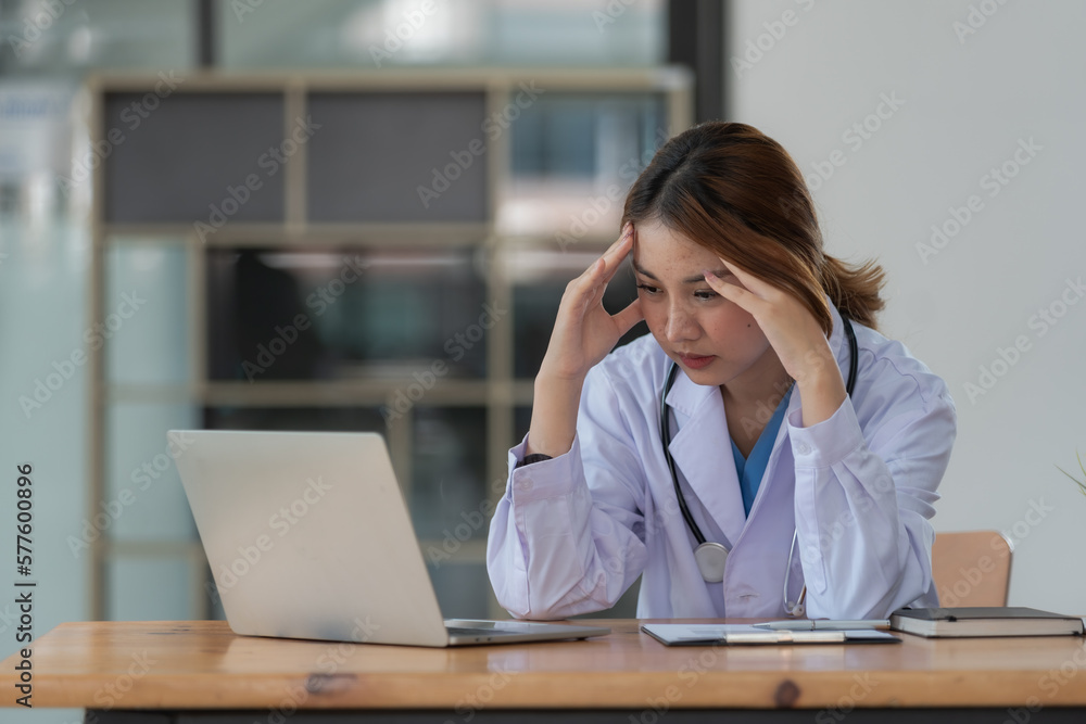 Shot of a mature doctor sitting alone in her clinic and feeling stressed while using her laptop. Shot of a mature doctor sitting alone in her clinic and feeling stressed while using her laptop.