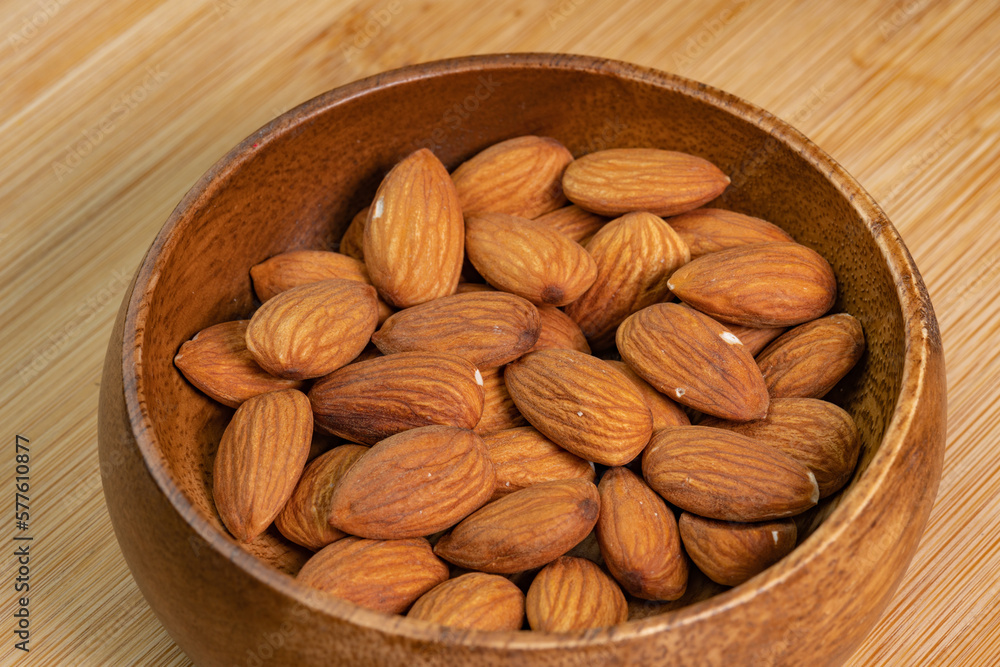 Almond nuts in wooden bowl on wooden background close up. Product rich in minerals and vitamins. Almond kernels. Healthy skin and hair and natural healing oil treatment Almond nuts in wooden bowl on wooden background close up. Product rich in minerals and vitamins. Almond kernels. Healthy skin and hair and natural healing oil treatment