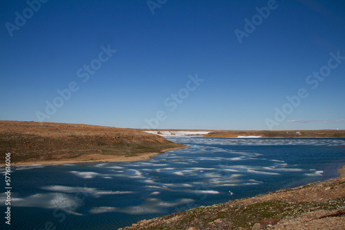 Arctic landscape in summer time. A river with broken ice flowing along a barren tundra. Near Cambridge Bay, Nunavut, Canada