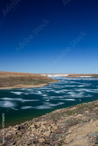 Arctic landscape in summer time. A river with broken ice flowing along a barren tundra. Near Cambridge Bay, Nunavut, Canada photo