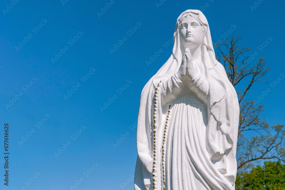 Virgin Mary sculpture against blue sky (concept of faith, death)