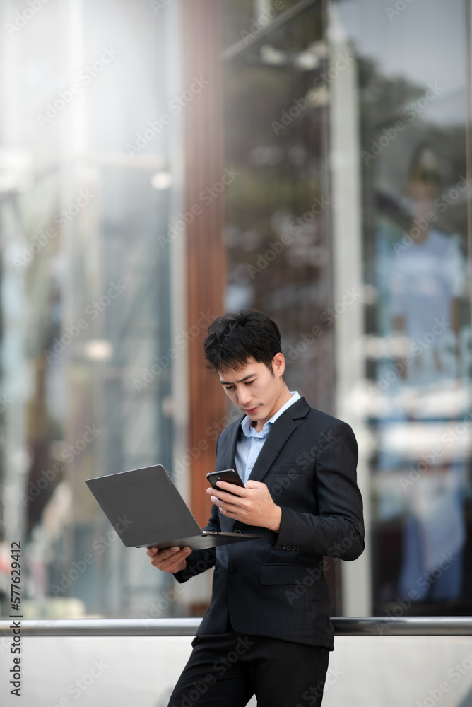 Asian businessman using a tablet and laptop on a bench in the city Asian businessman using a tablet and laptop on a bench in the city