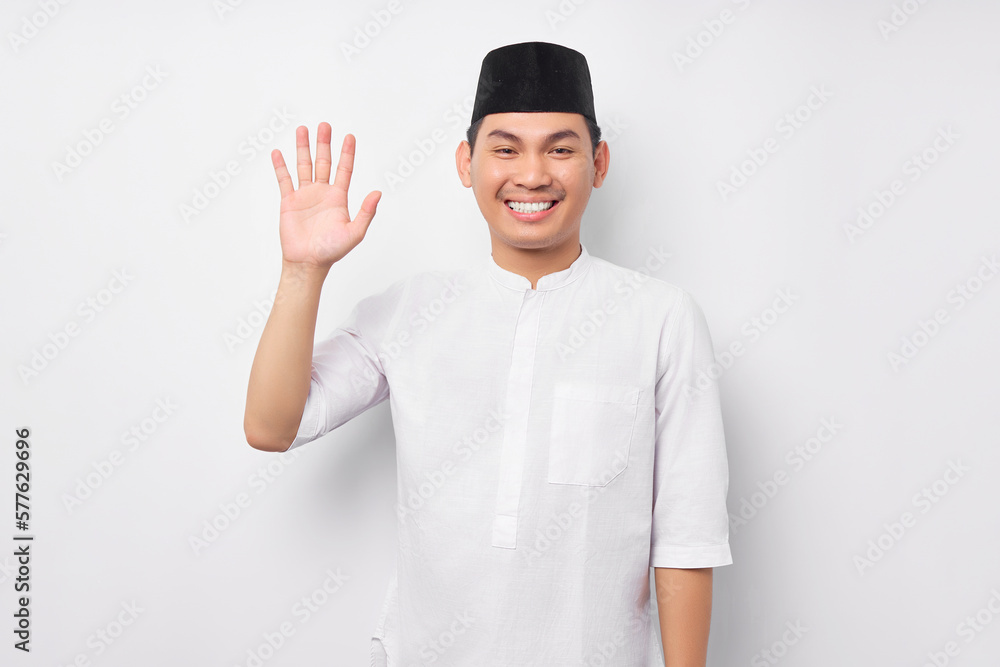 Smiling friendly young Asian Muslim man wearing Arabic costume tell say hello to camera and waving hand to greet someone isolated over white background. People religious Islamic lifestyle concept Smiling friendly young Asian Muslim man wearing Arabic costume tell say hello to camera and waving hand to greet someone isolated over white background. People religious Islamic lifestyle concept