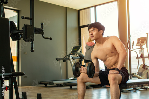 Asian handsome man using dumbbell for exercise to build arm muscles in the gym.