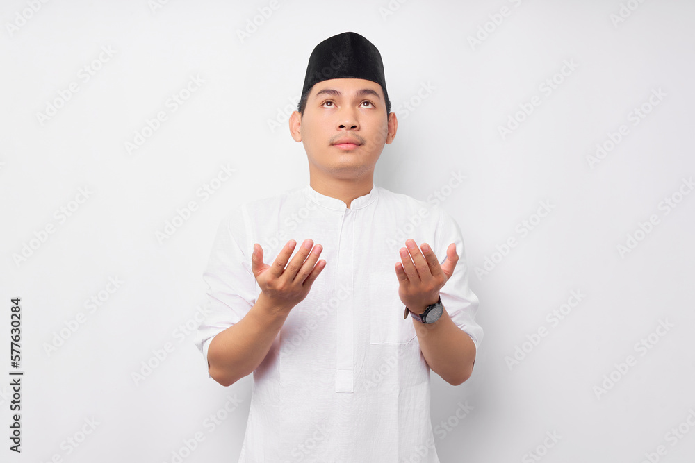 Handsome young Asian Muslim man in Arabic costume standing with raising hands and praying to god isolated on white background. People religious Islamic lifestyle concept Handsome young Asian Muslim man in Arabic costume standing with raising hands and praying to god isolated on white background. People religious Islamic lifestyle concept