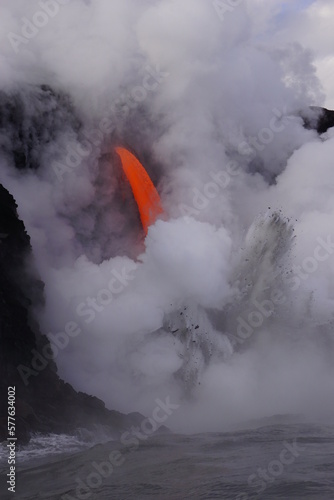 Lava flows down from high cliff into the ocean surrounded by white steam, Big Island in Hawaii