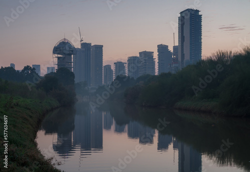 Tel Aviv skyline evening foggy view from Hayarkon park. Modern skyscrapers reflected in the forest river