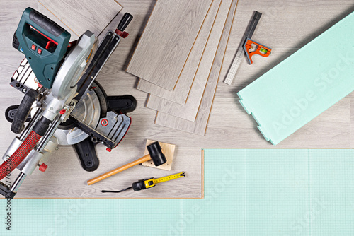 laying new laminate or vinyl flooring. Tools like chop saw hammer rolling measure gray laminate tiles on footstep sound insulation. diy professional home improvement renovation concept.