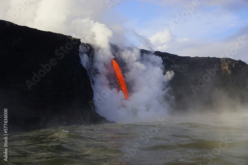 Stream of hot lava flowing down from high Cliff surrounded by white steam, Hawaii Big Island