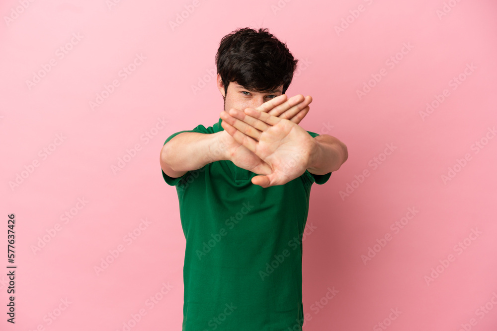 Young Russian man isolated on pink background making stop gesture with her hand to stop an act Young Russian man isolated on pink background making stop gesture with her hand to stop an act