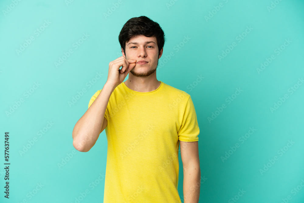 Young Russian man isolated on blue background showing a sign of silence gesture Young Russian man isolated on blue background showing a sign of silence gesture