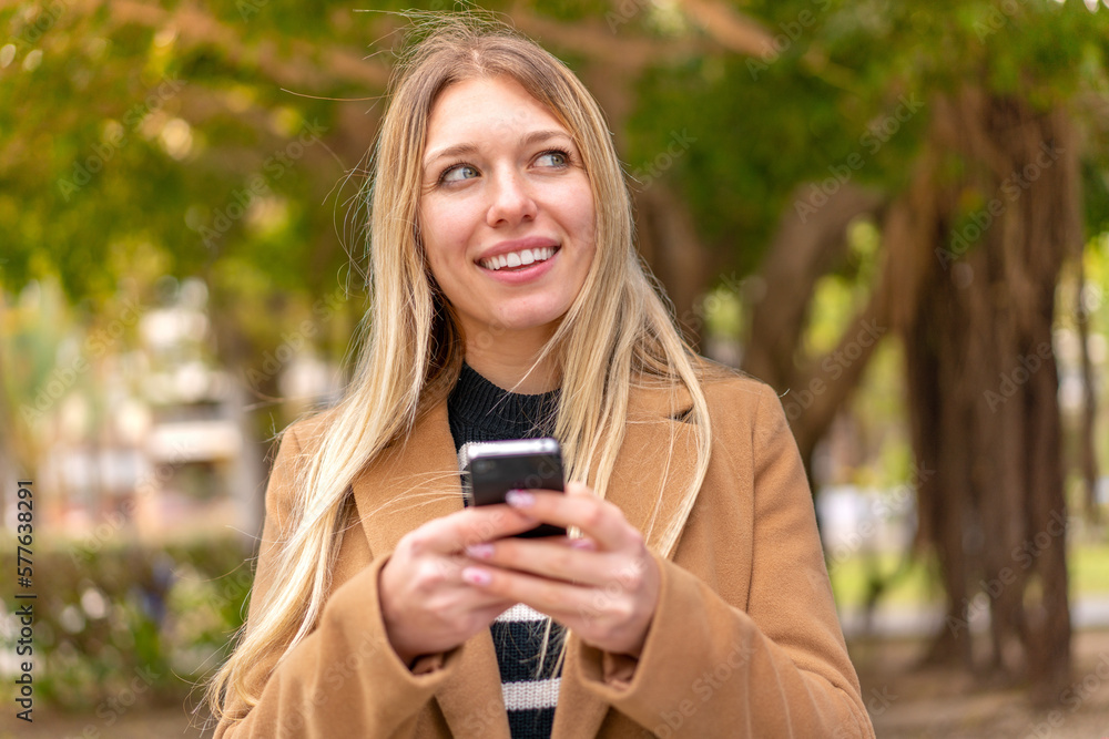 Young pretty blonde woman at outdoors using mobile phone and looking up Young pretty blonde woman at outdoors using mobile phone and looking up