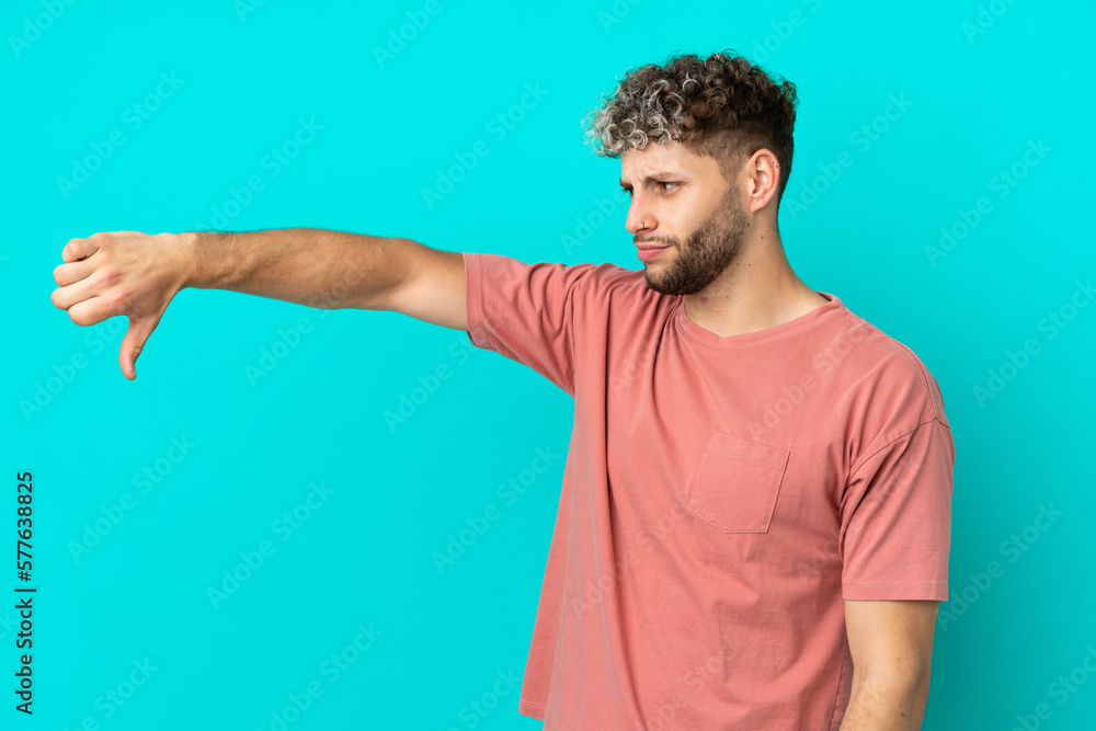 Young handsome caucasian man isolated on blue background showing thumb down with negative expression Young handsome caucasian man isolated on blue background showing thumb down with negative expression