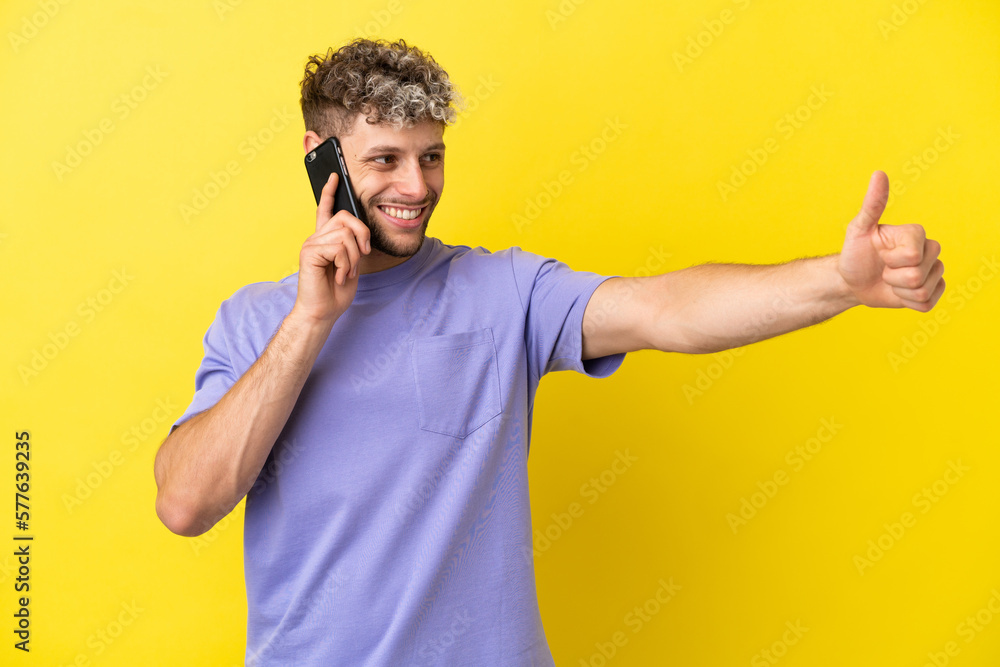 Young caucasian man using mobile phone isolated on yellow background giving a thumbs up gesture Young caucasian man using mobile phone isolated on yellow background giving a thumbs up gesture
