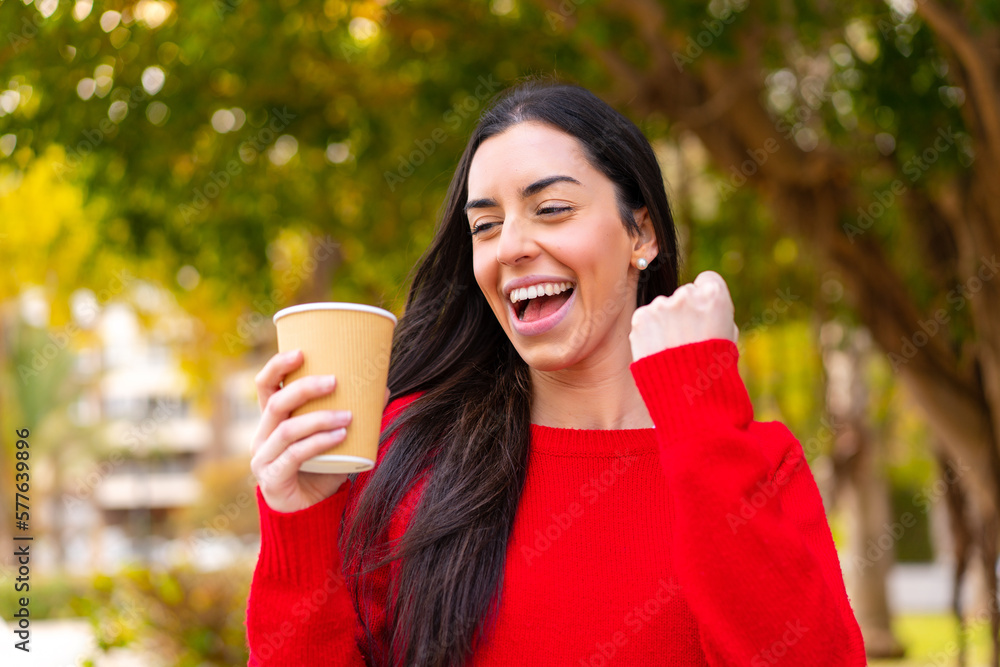 Young woman holding a take away coffee at outdoors celebrating a victory