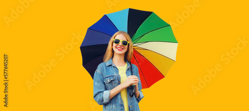 Portrait of happy smiling young woman with colorful umbrella isolated on yellow background