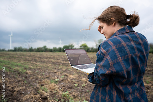 Farmer with laptop on the field. Wind turbines on a horizon. Smart sustainable farming and agriculture digitalization	
