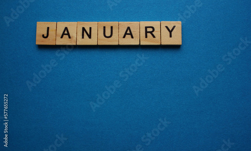 The word January is made of wooden cubes on a blue background. Winter month. Top view