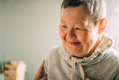 an elderly woman with Down syndrome, accompanied by an assistant who supports her, holds her hands