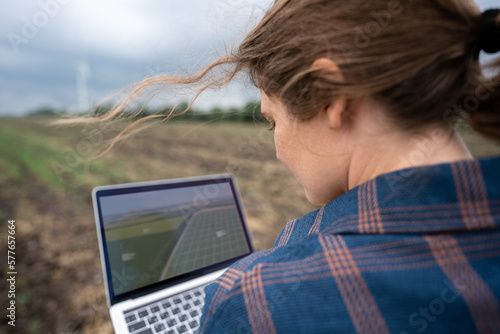 Farmer with laptop on the field. Wind turbines on a horizon. Smart sustainable farming and agriculture digitalization