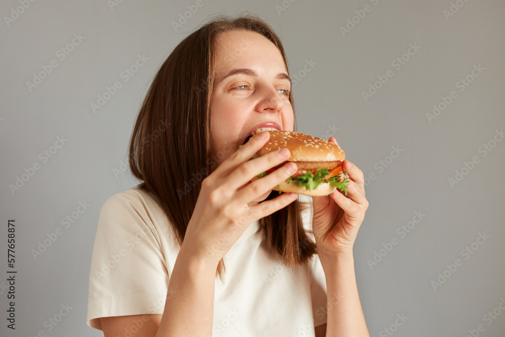 Profile portrait of Caucasian brown haired woman biting of appetizing delicious hamburger, being extremely hungry, enjoying junk food, finishing diet, having cheat meal. Profile portrait of Caucasian brown haired woman biting of appetizing delicious hamburger, being extremely hungry, enjoying junk food, finishing diet, having cheat meal.