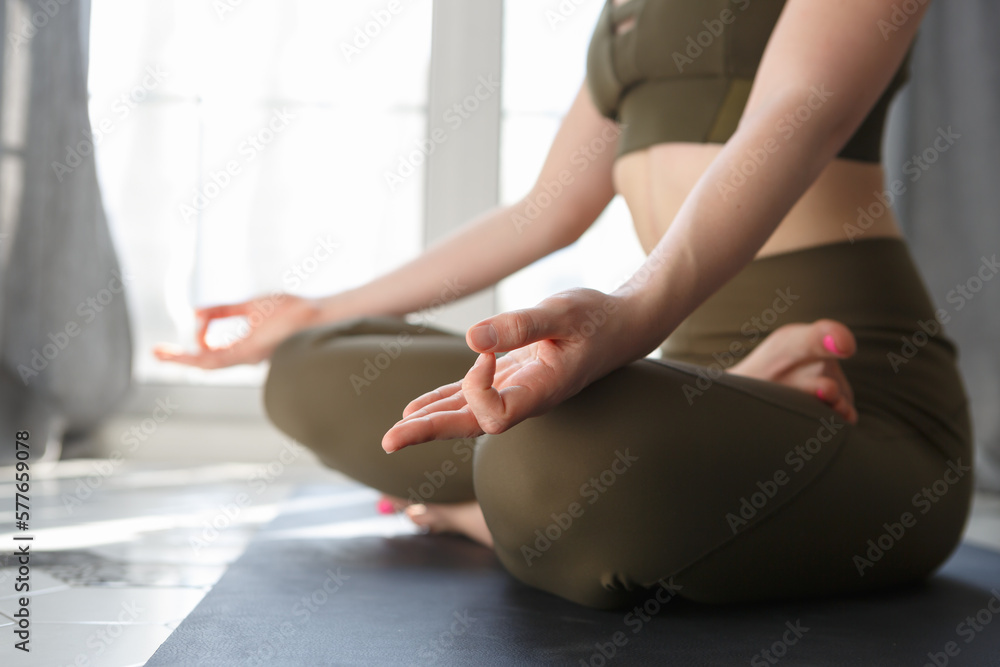Yogini girl doing meditation exercise in the morning. Unrecognizable young woman sitting in lotus pose an meditating.