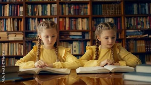 Focused sisters reading books in school library, identical twins, education