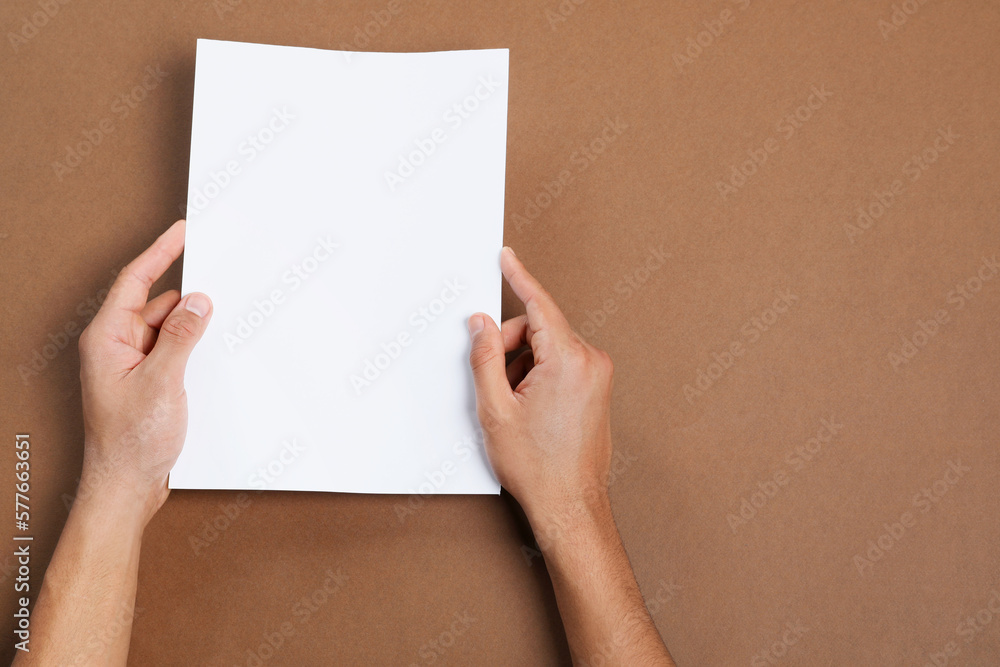 Man holding sheet of paper on brown background, closeup. Mockup for design Man holding sheet of paper on brown background, closeup. Mockup for design